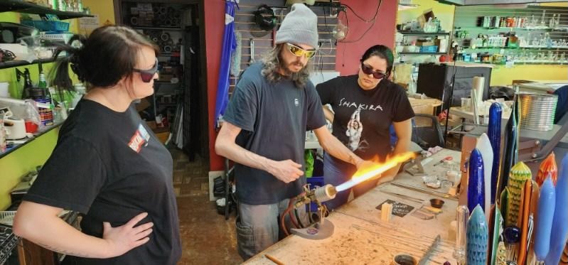 Three people learning at the torch during a glass blowing lesson