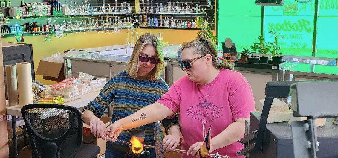 Two women learning glass blowing at a torch